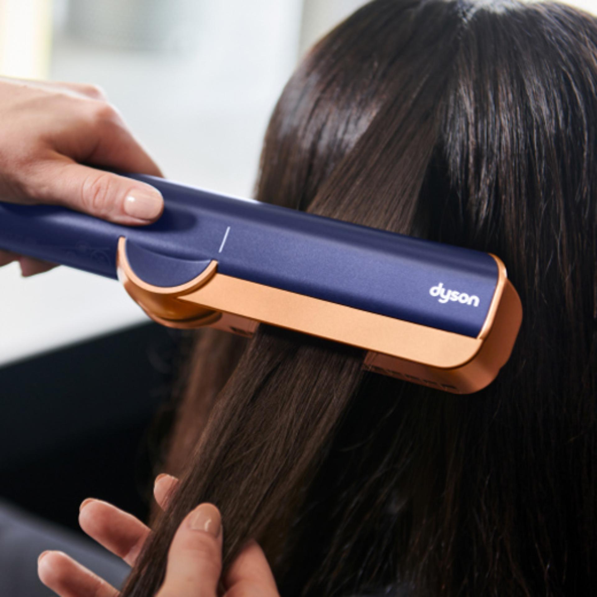 Close-up of the Dyson Airstrait straightener straightening long black hair.